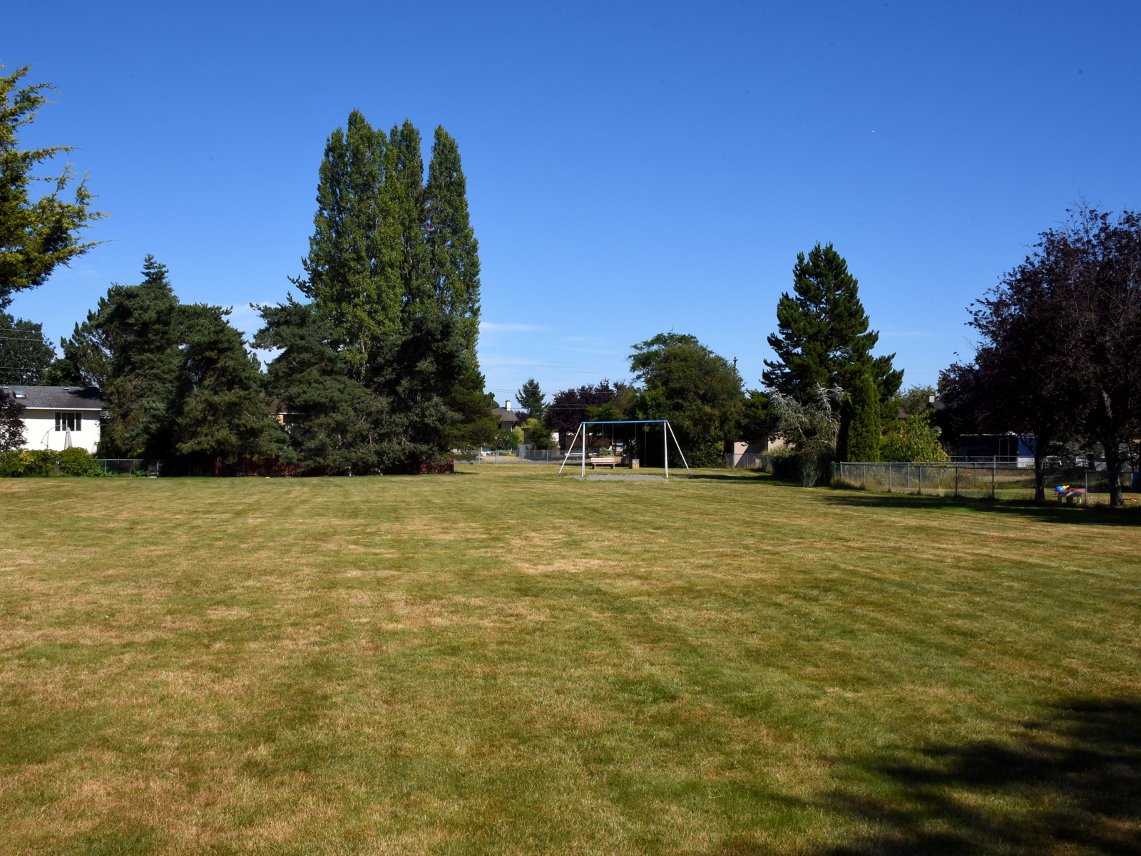 Image of Beaver Park with a grassy field and two swing swingset and a bench in the background.