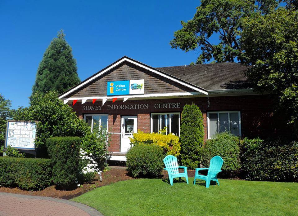 Image of the Sidney Visitor Information Centre, a red brick clad building located in Bevan Park, with two teal lawn chairs on the grass in front of the building