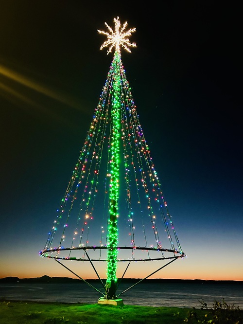 A big lit up star sits atop a Christmas tree made of lights, against the backdrop of an orange strip of sunset.