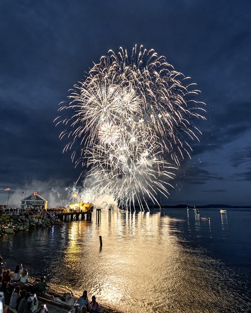 White fireworks against a dark sky over the Sidney waterfront, with the Beacon Wharf and